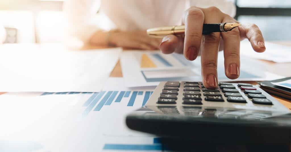 usinesswoman calculating project costs and cash flow on a laptop and calculator in an office.